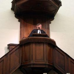 Pasteur en chaire, derrière les coupes de la Sainte Cène